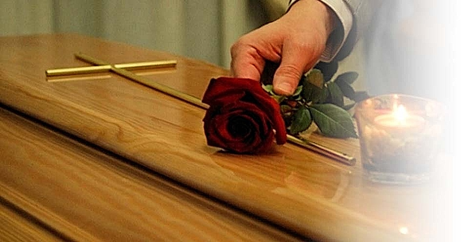 Una rosa rossa posata sul feretro accanto alla croce